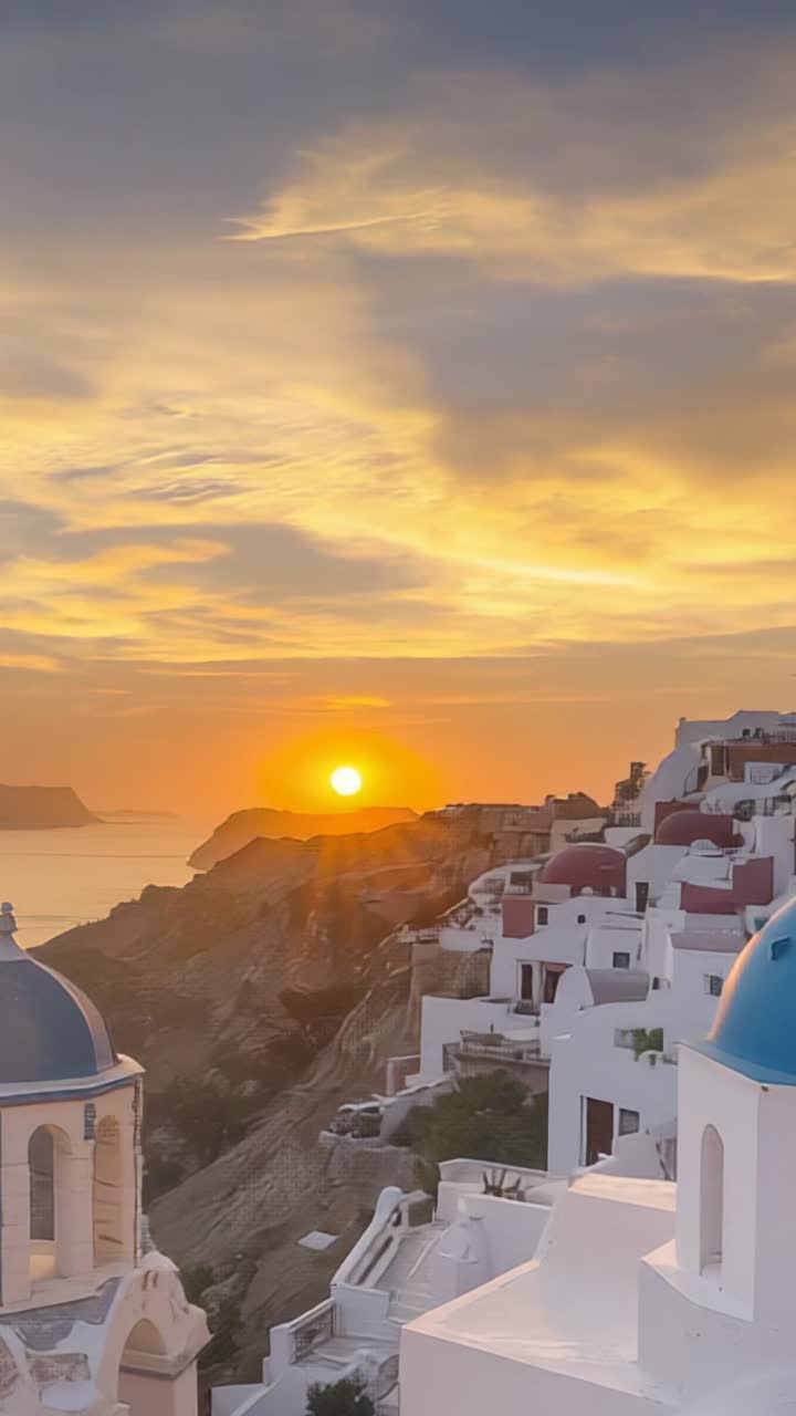 Vertical video: Rising sun above horizon bathing whitewashed blue-domed buildings on Aegean cliffs