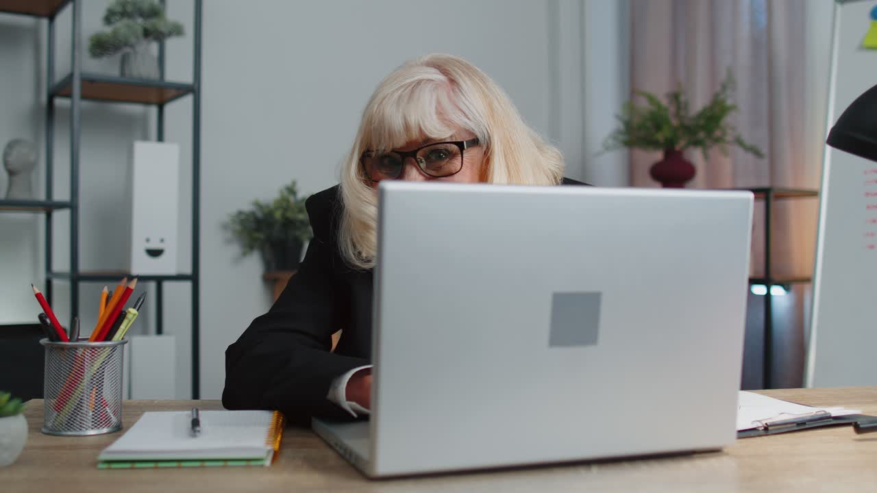 Senior mature older business woman hiding behind laptop computer making funny face fooling around