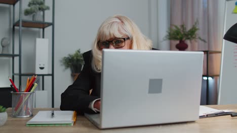 senior mature older business woman hiding behind laptop computer making funny face fooling around