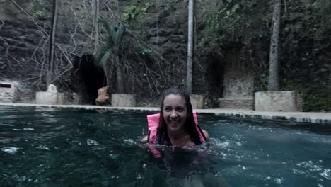 mujer caucásica saltando a una piscina natural fría con bosque en el fondo