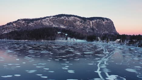 aerial view of a frozen lake at sunrise with long cracks and circular patterns flying towards an isolated mountain