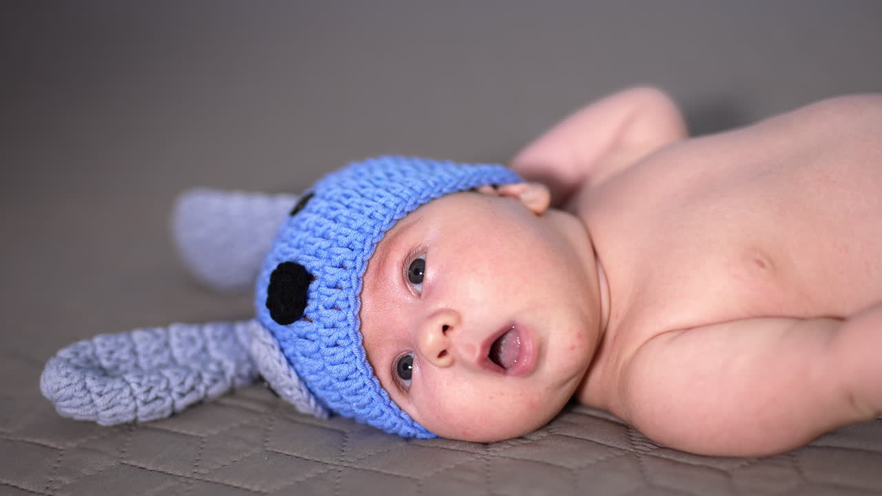 Cute toddler in a funny cap with ears on the bed. Naked child in a hat only lying on the bed and looking up. Close up.