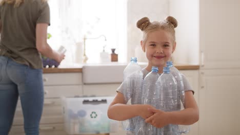 Portrait-video-of-smiling-girl-holding-plastic-bottles-in-kitchen