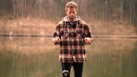 A-young-man-standing-next-to-a-beautiful-background,-where-the-water-mirrors-the-forest-behind