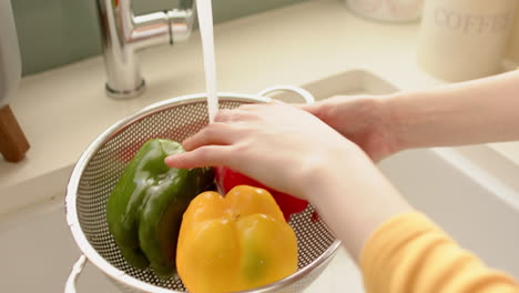 washing colorful bell peppers in colander under running water in kitchen sink