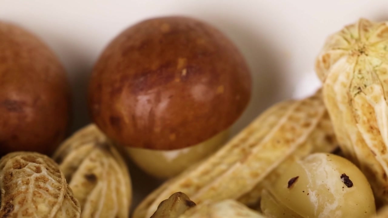 A detailed macro view of textured peanut shells and smooth chestnuts in a bowl.
