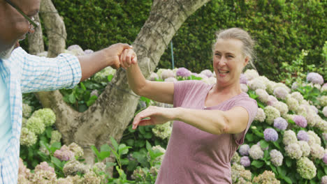 Glückliches-älteres,-Vielfältiges-Paar,-Das-Hemden-Trägt-Und-Im-Garten-Tanzt