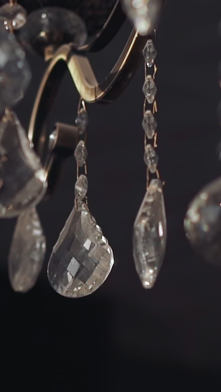 Shiny transparent drop shaped crystal ornate on vintage chandelier in semi-dark room closeup. Home decor classic element. Design ideas for interior