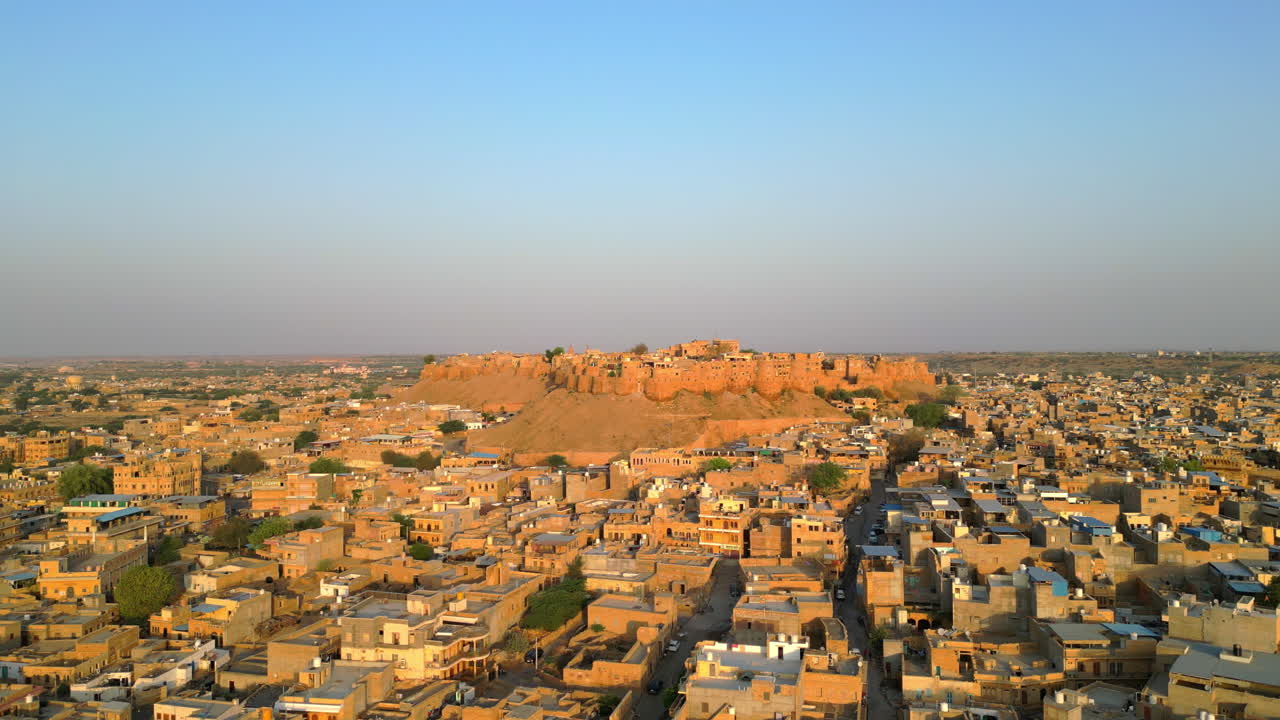 A breathtaking 4K orbit drone shot of Jaisalmer Fort, surrounded by traditional Rajasthani houses. The intricate architecture with the vibrant desert hues under a clear blue sky India