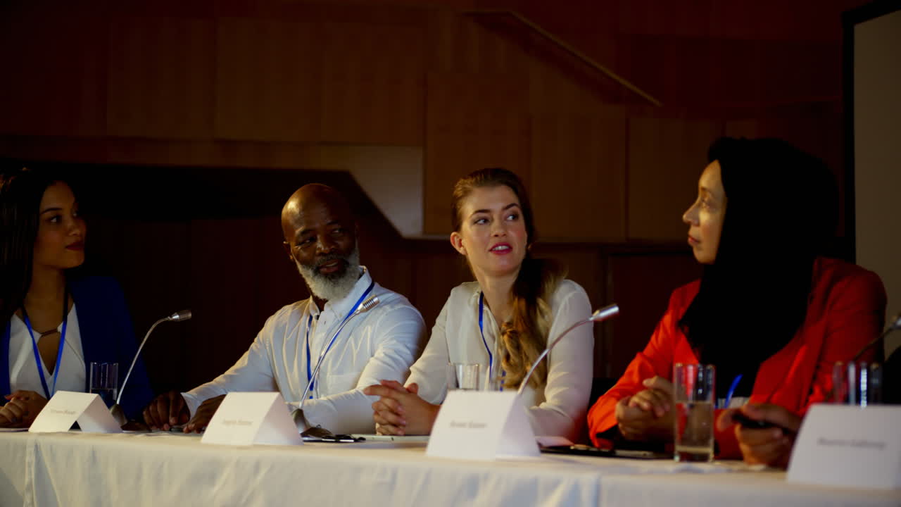 Multi-ethnic business people sitting at table in business seminar in auditorium 4k