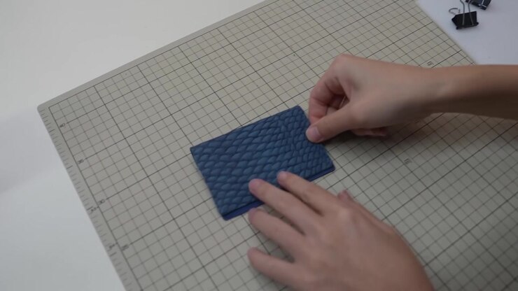 Hands shape folded blue leather pouch into its final form