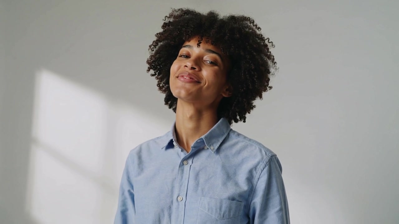 Smiling woman in light blue shirt responding to prompt in studio tilting head, with window light