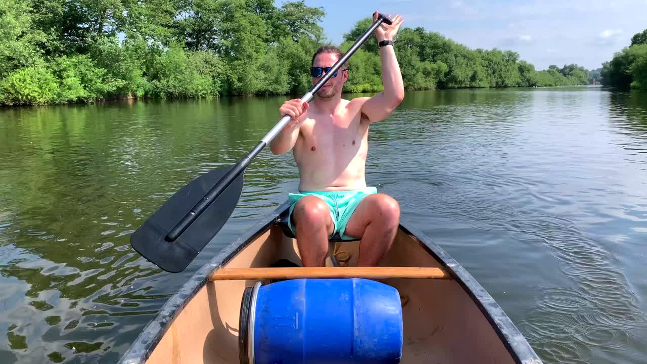 hombre en topless rema en canoa en el río wye al sol a lo largo de la orilla del río verde