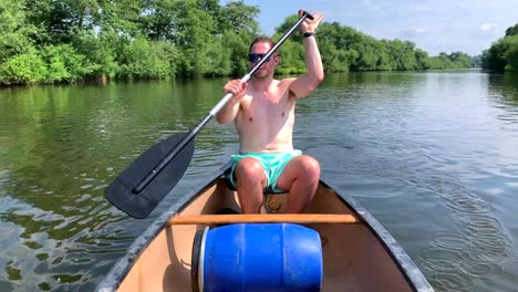 Topless-man-paddles-canoe-on-river-wye-in-sun-along-green-river-bank