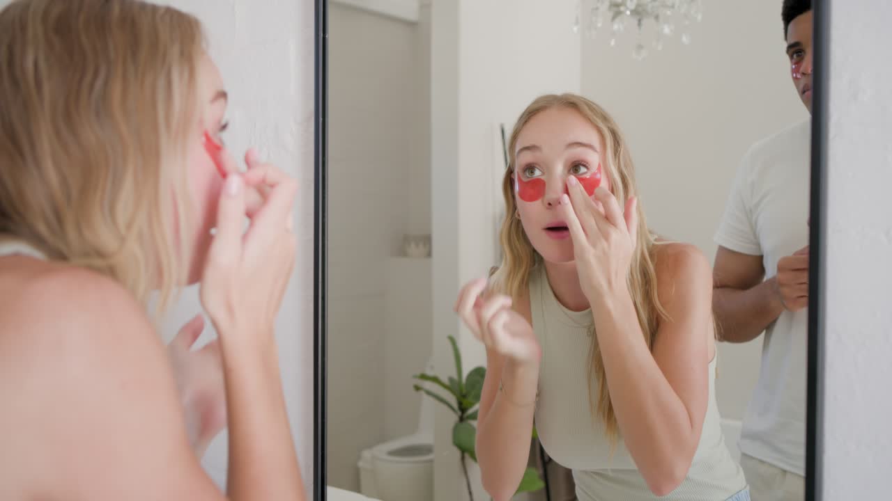 Coppia allo specchio, donna in top senza maniche che prende un barattolo, applicando patch rossi per gli occhi per la cura della pelle.