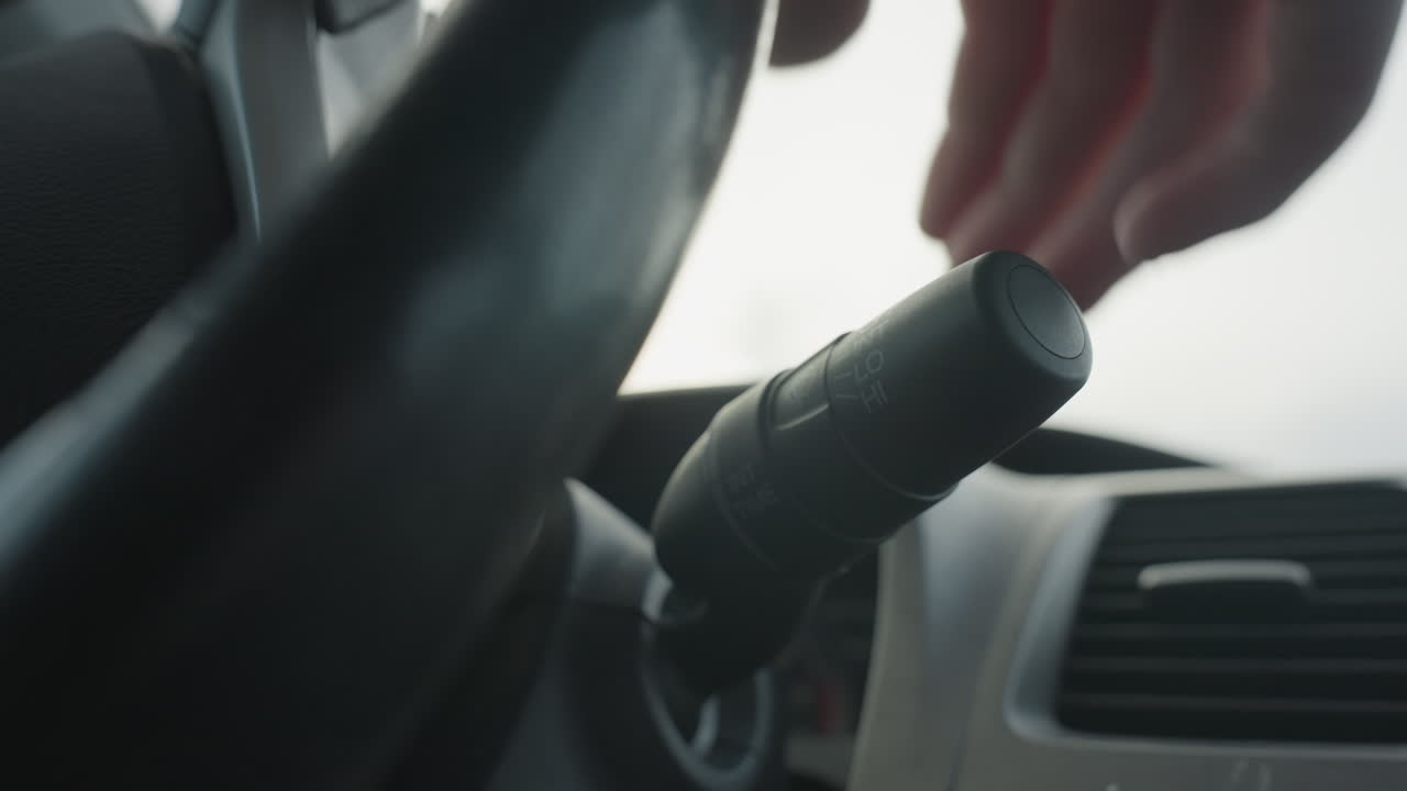 Close up of person lifting windshield wiper control lever and adjusting knob settings inside car interior showing hand interaction with automotive mechanism during manual operation