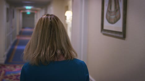 Attractive-woman-in-blue-dress-searching-room-in-corridor-apartment-hotel