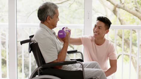 diverse male physiotherapist advising and senior man in wheelchair using dumbbells, in slow motion