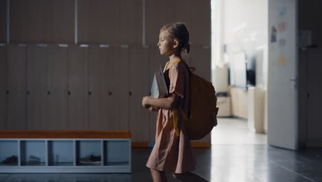 Schoolgirl-walking-holding-books-in-empty-hall-alone.-Pupil-passing-classrooms.