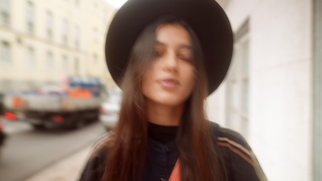 Giovane donna con cappello che sorride in una strada di città con effetto mosso