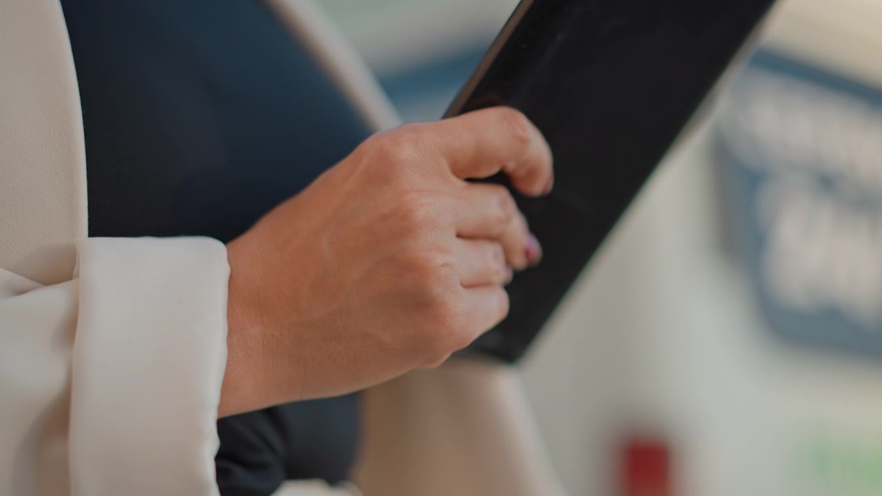 Vista ravvicinata di mani che stringono uno smartphone nero vicino al petto, con un sottile gesto di sollevamento, inclinazione e rotazione che suggerisce di controllare lo schermo, leggere notifiche, toccare e rimanere connessi al chiuso.
