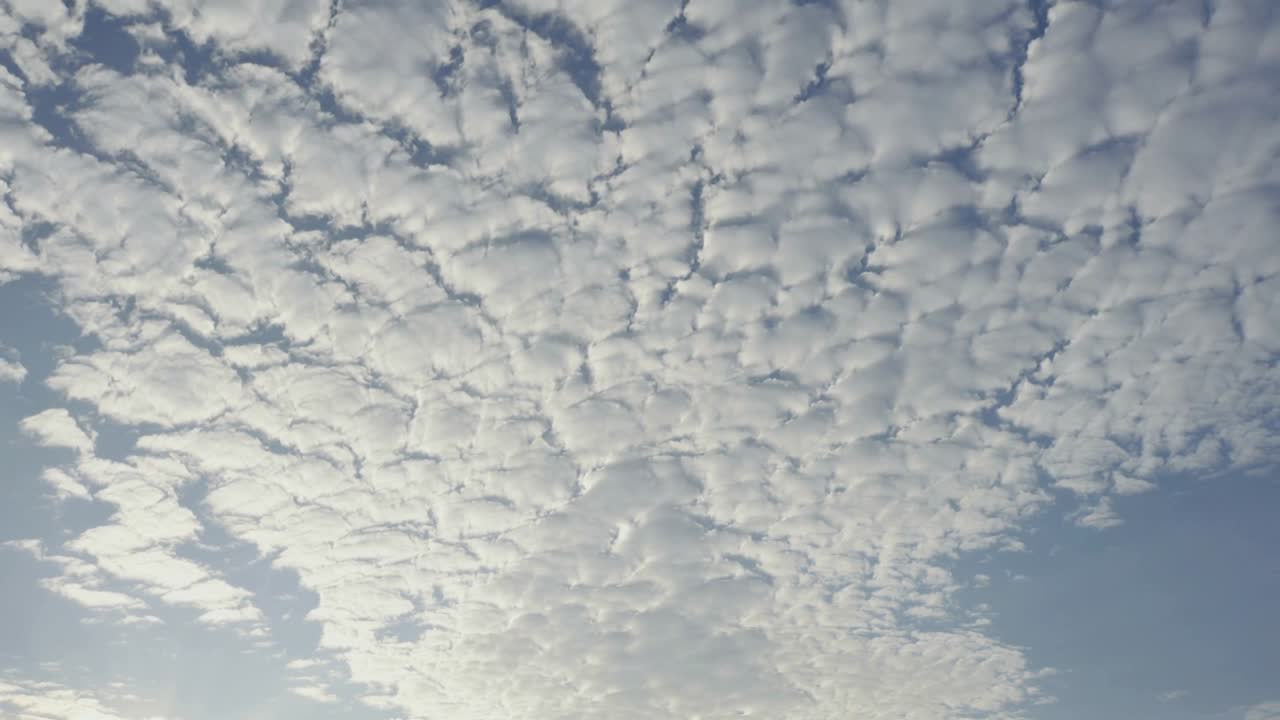 Couche de nuages altocumulus dérivant et se déplaçant dans le ciel bleu, le vent éclaircissant un coin ensoleillé.