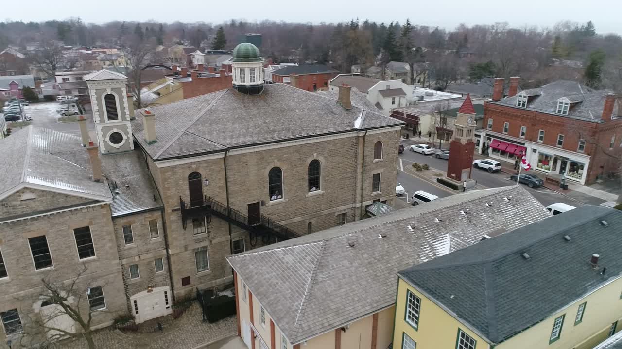 A drone captures an aerial view of Niagara-on-the-Lake's downtown courthouse, on a quaint old street filled with shops, as light snow falls in winter
