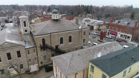 un avión no tripulado captura una vista aérea del juzgado del centro de niagara-on-the-lake, en una pintoresca calle vieja llena de tiendas, mientras cae una nieve ligera en invierno