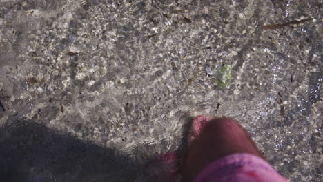 un homme portant un short rose marche pieds nus dans l'eau de mer peu profonde