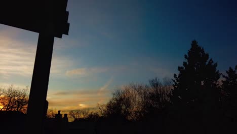 wide time-lapse of winter sunset from the balcony of a house, panning left to right, with fast moving clouds and trees moving in the wind