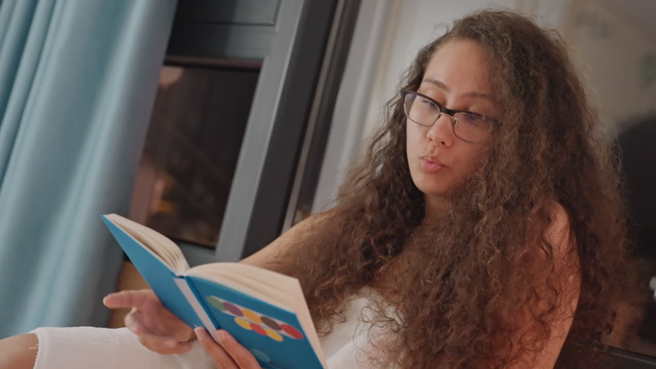 Lectrice près de la fenêtre. Une session de lecture captivante avec un éclairage doux et une ambiance calme. Hôte raconte avec enthousiasme une histoire dans une chambre d'hôtel éclairée par des lumières tamisées et une atmosphère tranquille.