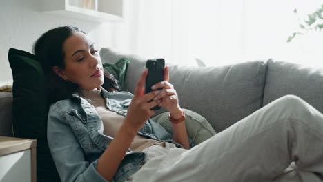 woman, thinking and typing on smartphone on sofa