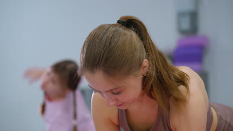 close-up of a gym instructor guiding children in an arm stretch exercise during a workout session, with one child slightly blurred in the foreground
