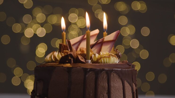 Photo de studio : gâteau d'anniversaire au chocolat décoré avec bougies allumées soufflées, fond lumineux bokeh.