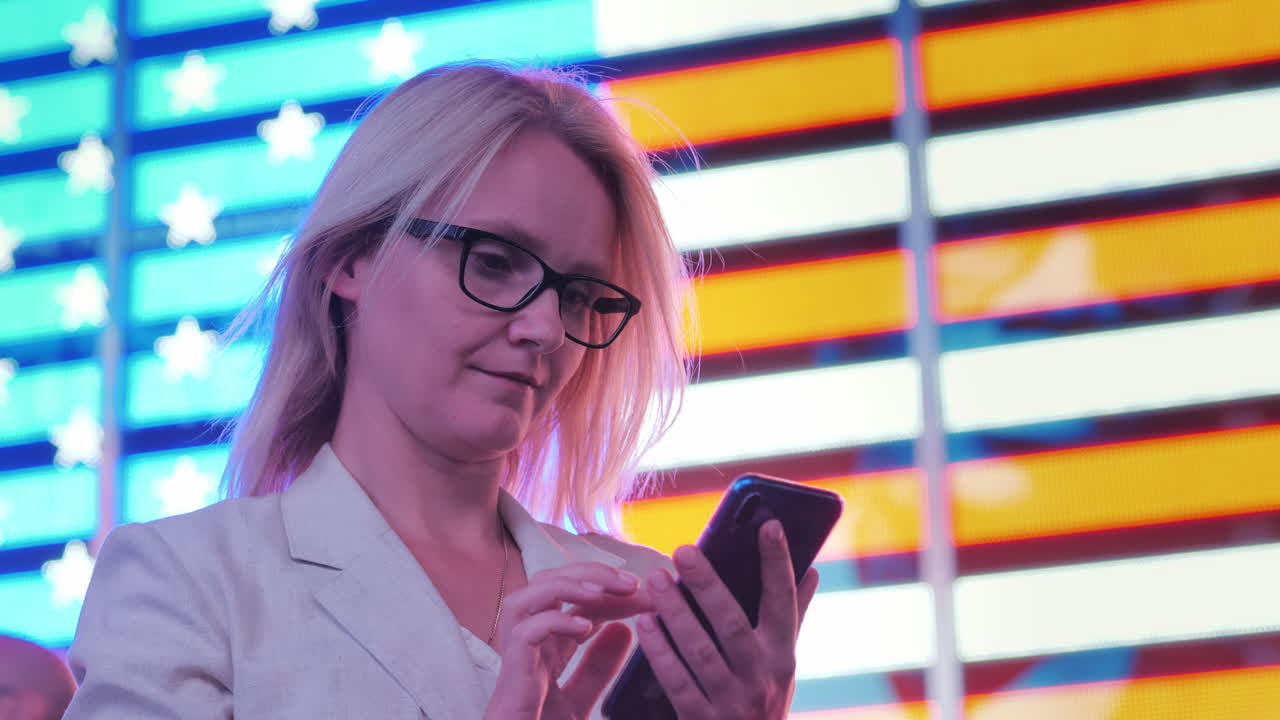 mujer de negocios usa un teléfono inteligente en el fondo de una gran bandera americana en el famoso times squa