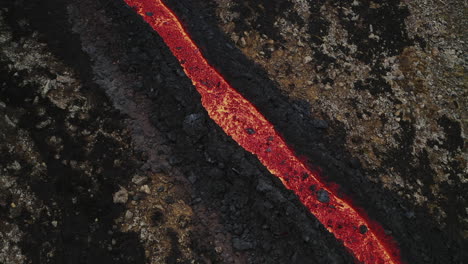 orange glowing stream of volcanic lava flowing down rocky hill