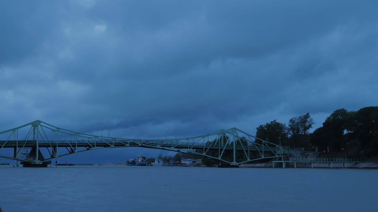 lapso de tiempo de hermosas nubes de lluvia gris oscuro en movimiento rápido sobre el puente oscilante oskara kalpaka en la ciudad de liepaja en la noche, plano general