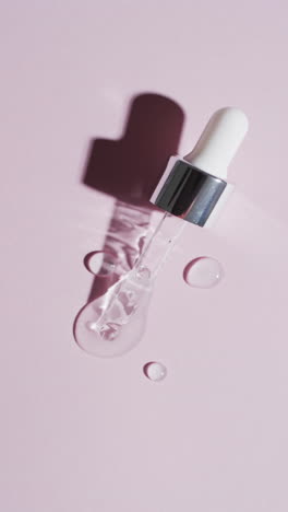 vertical video of make up pipette and drops of serum with copy space on pink background
