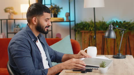 Indian-man-freelancer-closing-laptop-after-finishing-work-celebrating-success-victory-in-office-room