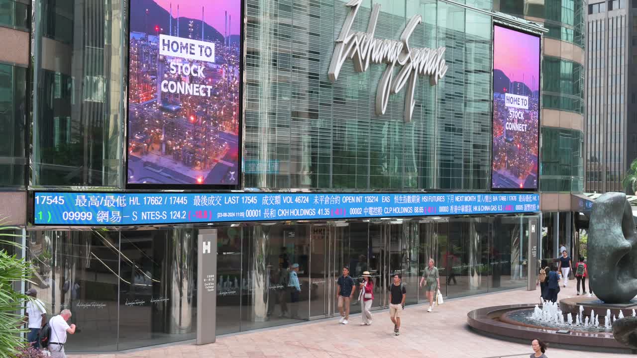 At the financial hub, businesspeople and pedestrians walk past the Exchange Square Complex (HKEX), home to the Hong Kong Stock Exchange, while negative stock ticker symbols are displayed on a screen.