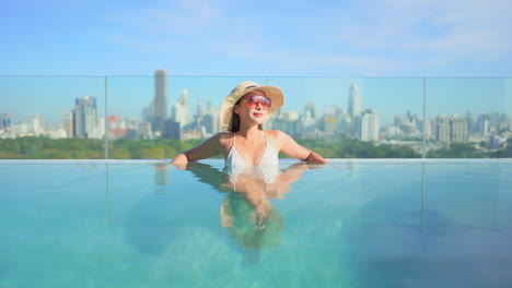 woman enjoying rooftop swimming pool with view of bangkok city skyline in the background