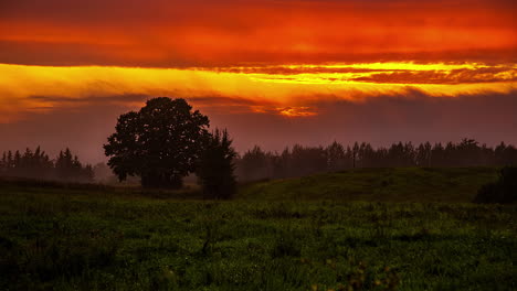 Static-shot-of-sunset-in-timelapse-through-dark-clouds-over-green-grassland-during-spring-day-at-sunset