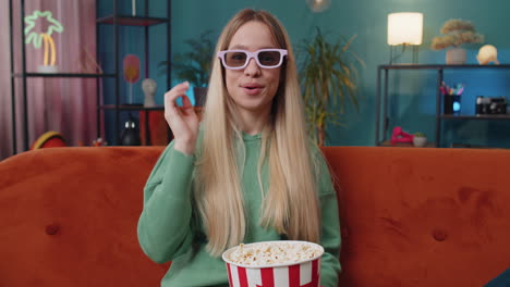 young woman sit on couch eating popcorn and watching interesting tv serial sport game online at home