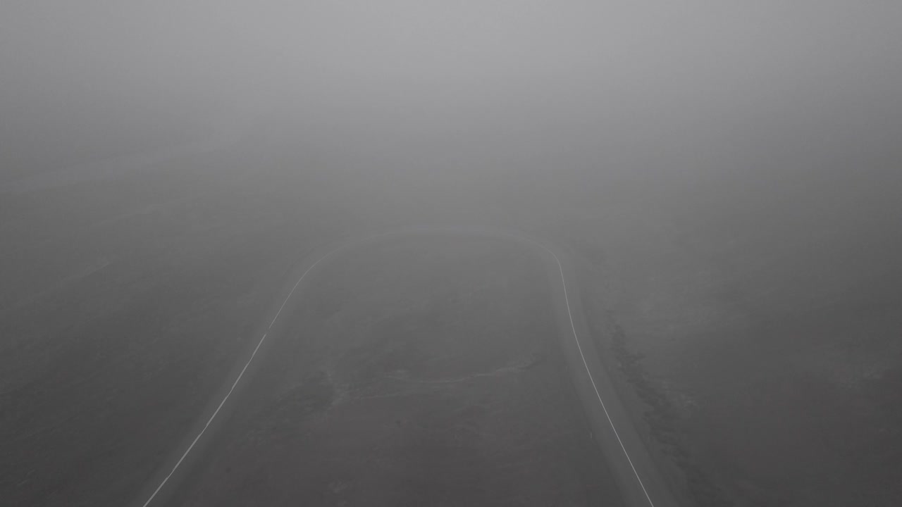 아이슬란드의 안개가 자욱하고 극적인 풍경 속에서 구불구불한 도로를 타고 내려가는 스케이터의 드론 샷