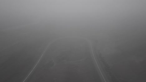 Drone-shots-of-skater-going-downhil-on-curvy-road-in-a-foggy,-dramatic-landscape-in-Iceland