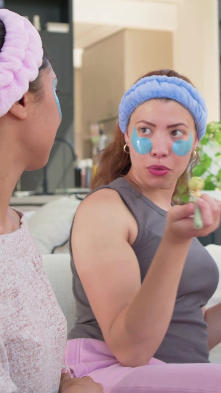 Vertical video: Talking woman in blue band and eye patches at home after tap, pointing for skincare