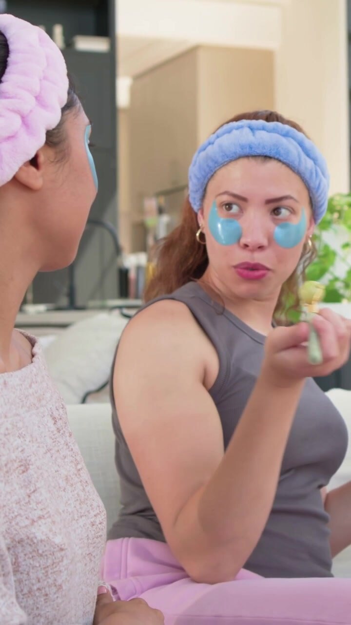 Vertical video: Talking woman in blue band and eye patches at home after tap, pointing for skincare