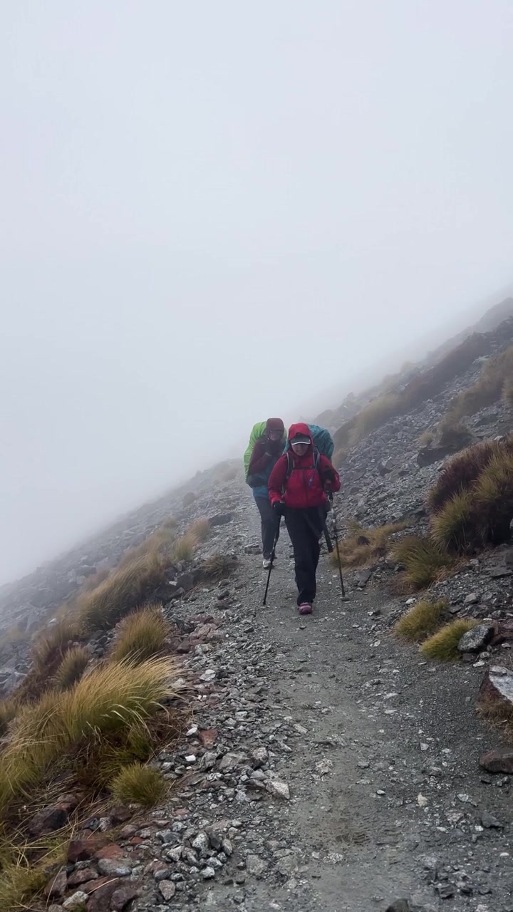Filmato verticale di due escursionisti con zaino che percorrono un sentiero alpino roccioso e nebbioso con bastoncini da trekking sul sentiero Kepler