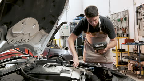 mecánico de automóviles masculino hispano revisando el automóvil con un lector de diagnóstico computarizado