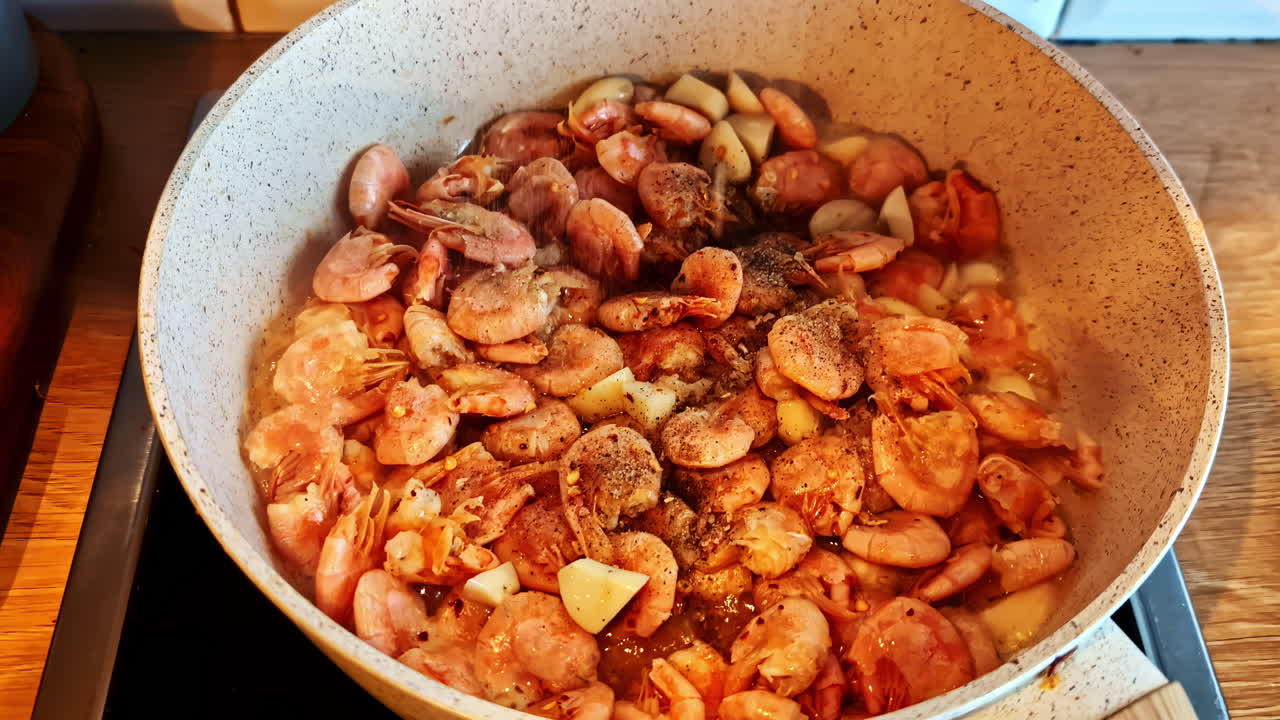 Close-up of cooked shrimp and garlic simmering in spiced oil in ceramic pan
